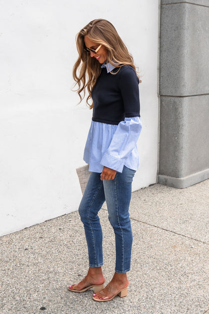 Woman in jeans and the Steve Madden Lenny Top - Navy smiles, holding a white clutch, standing against a white wall.