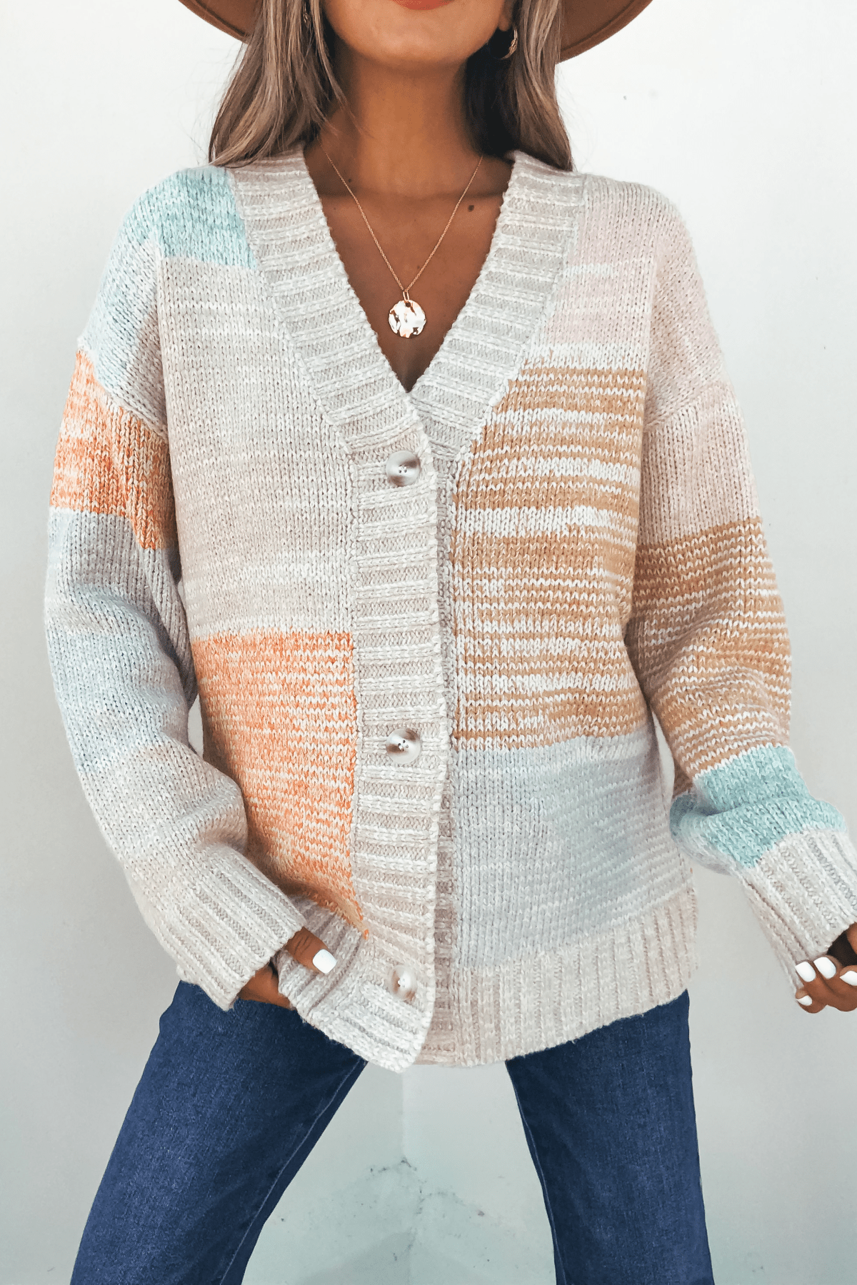 Woman in an Oatmeal Color Block Button Down Cardigan, blue jeans, hat, and necklace against a plain background.