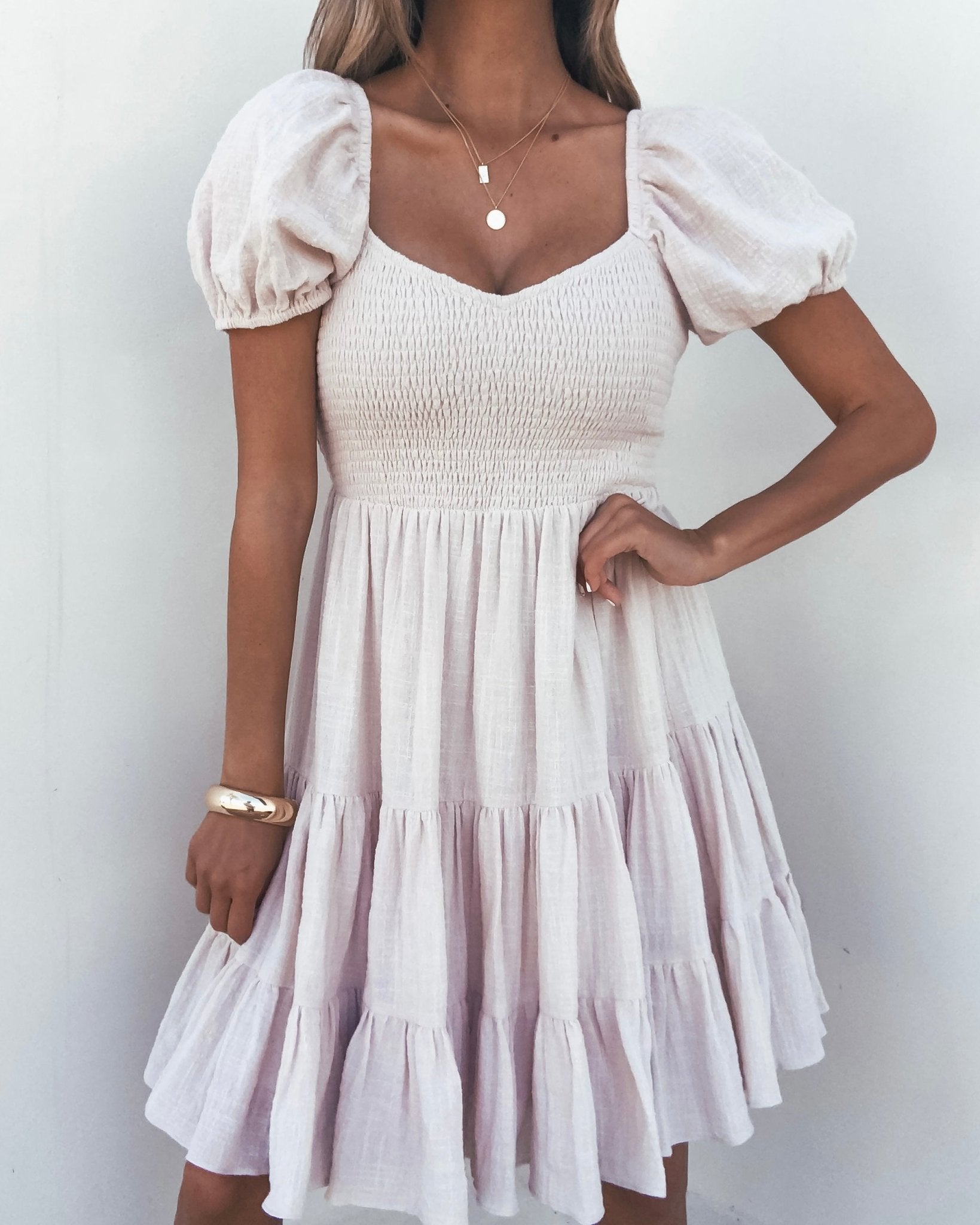 Woman wearing the Oatmeal Puff Sleeve Tiered Mini Dress, styled with necklaces and a bracelet.