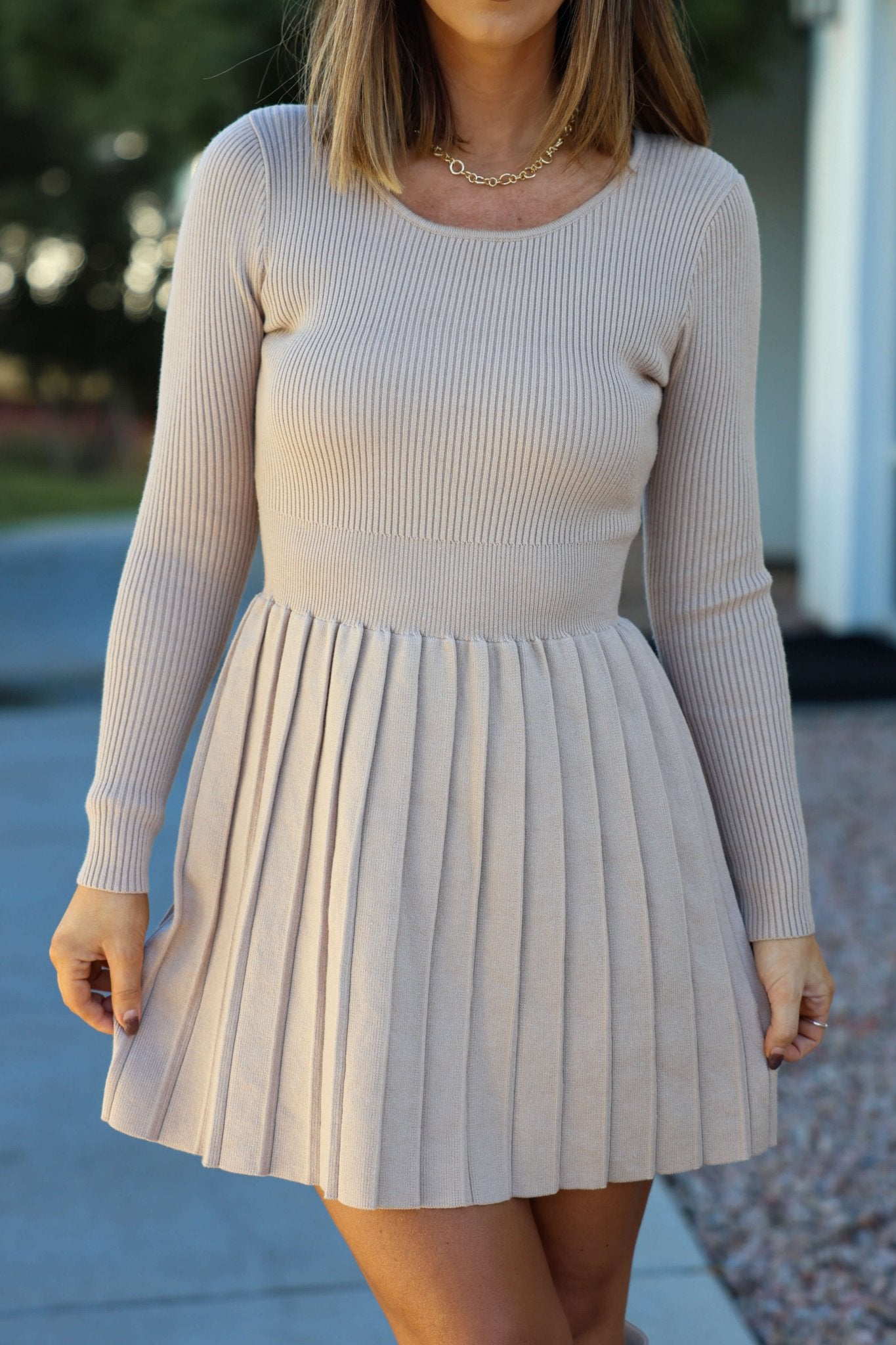 A woman stands outdoors in an Oatmeal Rib Knit Pleated Mini Dress with a fitted silhouette.