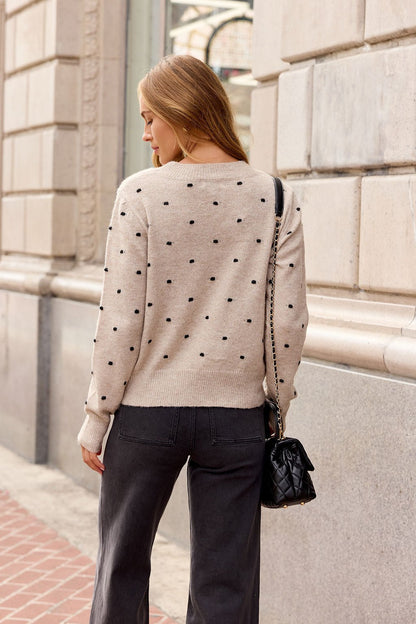 Woman with long hair in an Oatmeal Ribbed Polka Dot Sweater, black bag, and dark pants—perfect for fall—in the city.