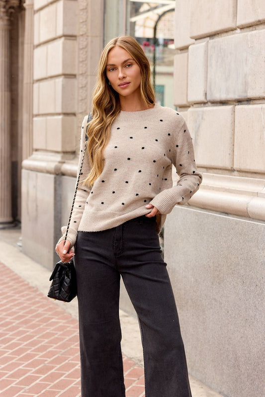 Woman in an oatmeal ribbed polka dot sweater and black pants with a quilted purse—perfect for fall sidewalk strolls.