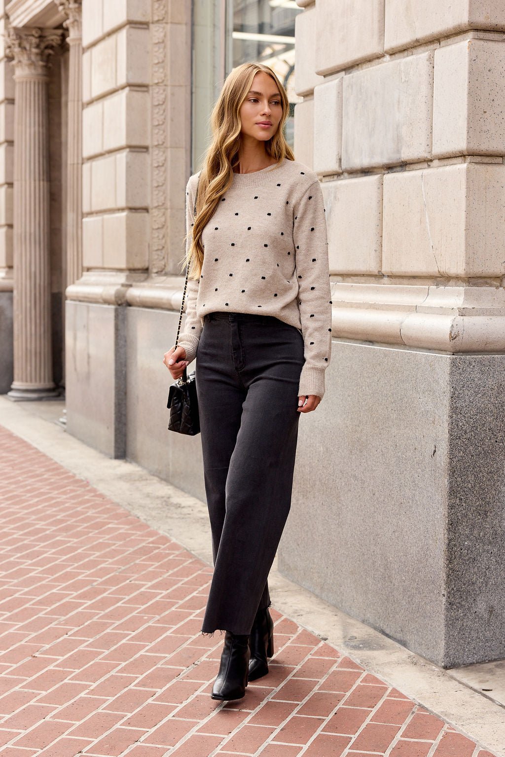 Woman walks city sidewalk in an Oatmeal Ribbed Polka Dot Sweater, black jeans, boots—perfect fall layers with her small black purse.