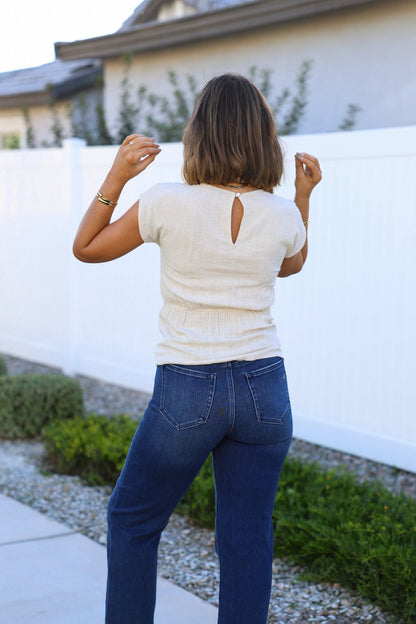 A woman in an Oatmeal Shirred Linen Top and blue jeans stands outdoors with her back to the camera.