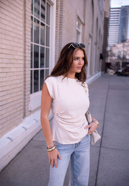 Woman in an Oatmeal Shirred Linen Top and light blue jeans stands on a city sidewalk, perfect for warm-weather styling.