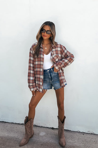 Woman in sunglasses, Off The Grid Plaid Flannel Shirt - Red, denim shorts, and cowboy boots poses confidently against a white wall.