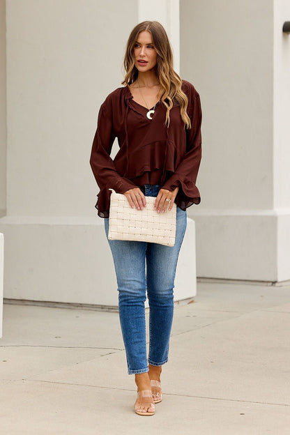 Woman in blue jeans, sandals, and the Office Bell Sleeve Top - Brown holds a woven clutch, standing out on the light sidewalk.
