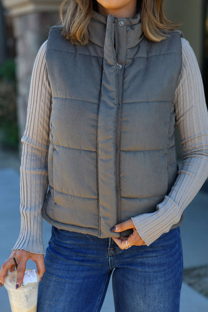 Wearing the Olive Button Up Puffer Vest, striped long-sleeve, and jeans—an ideal autumn layering look with an iced drink in hand.