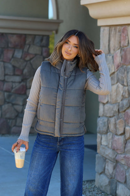 Woman in an olive button-up puffer vest and jeans, holding a drink—perfect for chic autumn outfits and fall layering.