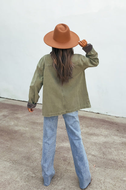 Person with long hair in a brown hat and blue jeans wears the Olive Contrast Collared Jacket, standing on concrete facing away.