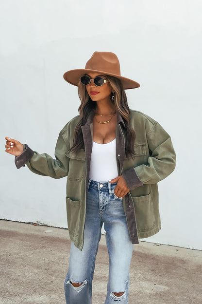 Woman in olive Contrast Collared Jacket, tan hat, sunglasses, white top, and ripped jeans stands outdoors by a light wall.