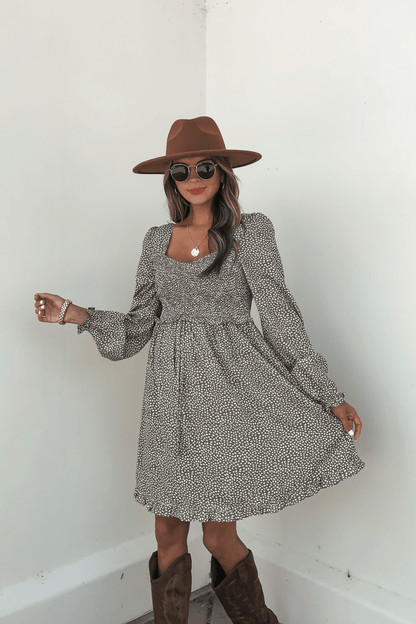 Woman wearing sunglasses, a brown hat, and the Olive Floral Print Ruched Mini Dress - FINAL SALE poses stylishly against a white wall.