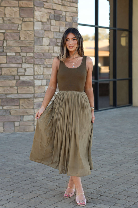 Woman wears Olive Scoop Neck Pleated Tank Midi Dress, standing by a stone building in sandals and layered necklaces.