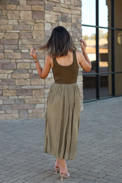 Woman in the Olive Scoop Neck Pleated Tank Midi Dress walks a stone path, facing away and flipping her hair.