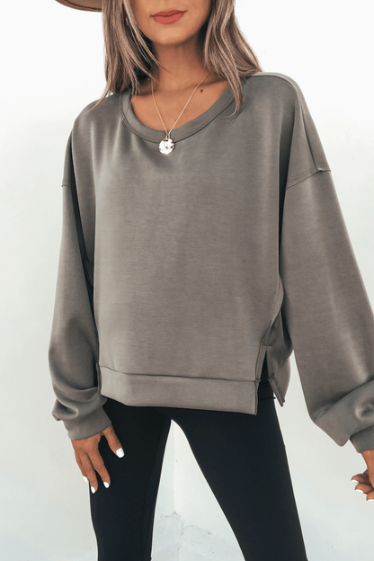 A woman in an oversized gray Olive Soft Cloud Scuba Top, black leggings, and a hat stands against a white background.