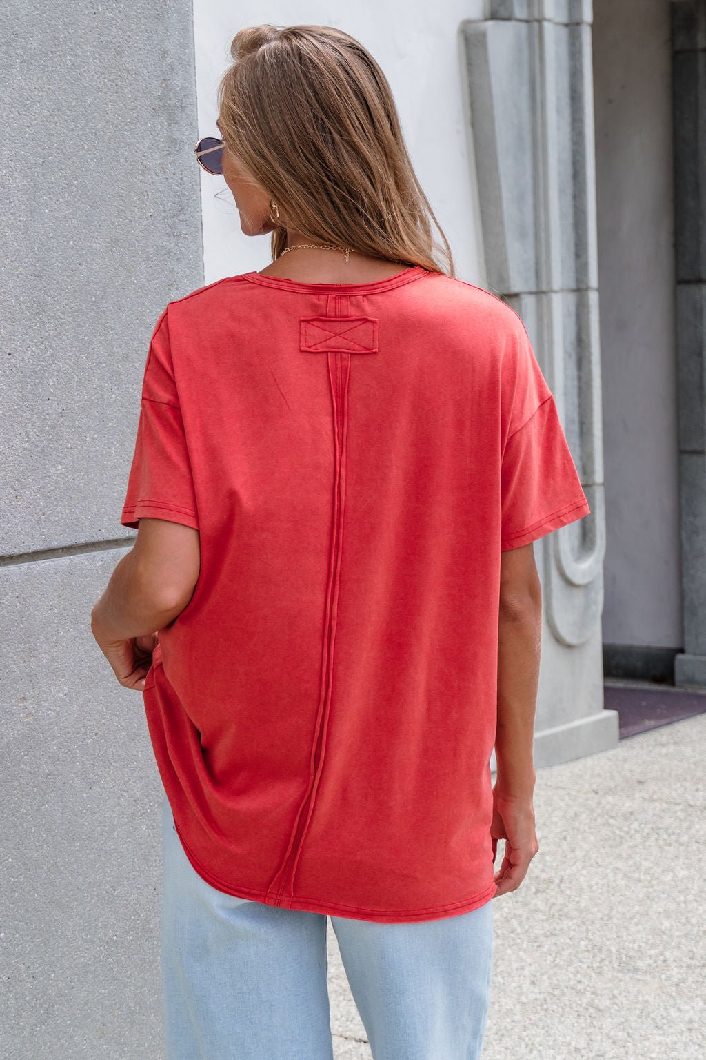 Someone in a red Oversized Graphic Tee and light blue jeans stands outdoors, facing away from the camera.