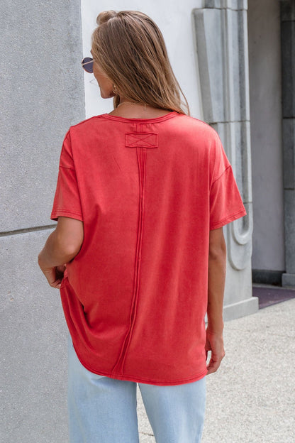 Someone in a red Oversized Graphic Tee and light blue jeans stands outdoors, facing away from the camera.