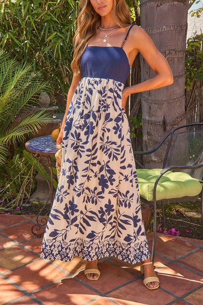 A woman in a Palm Beaded Strap Maxi Dress - Navy stands on a patio near outdoor furniture and lush green plants.