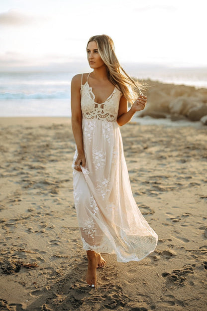 A woman walks barefoot on the beach at sunset in the Paradise Island Scalloped Vanilla Lace Maxi Dress.