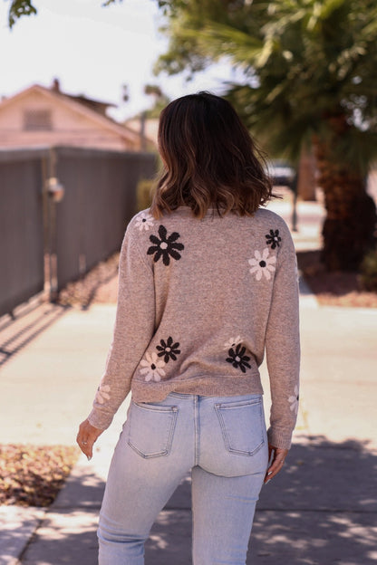 A woman in a Penelope Mocha Flower Detail Sweater and light jeans strolls down a sunny sidewalk.