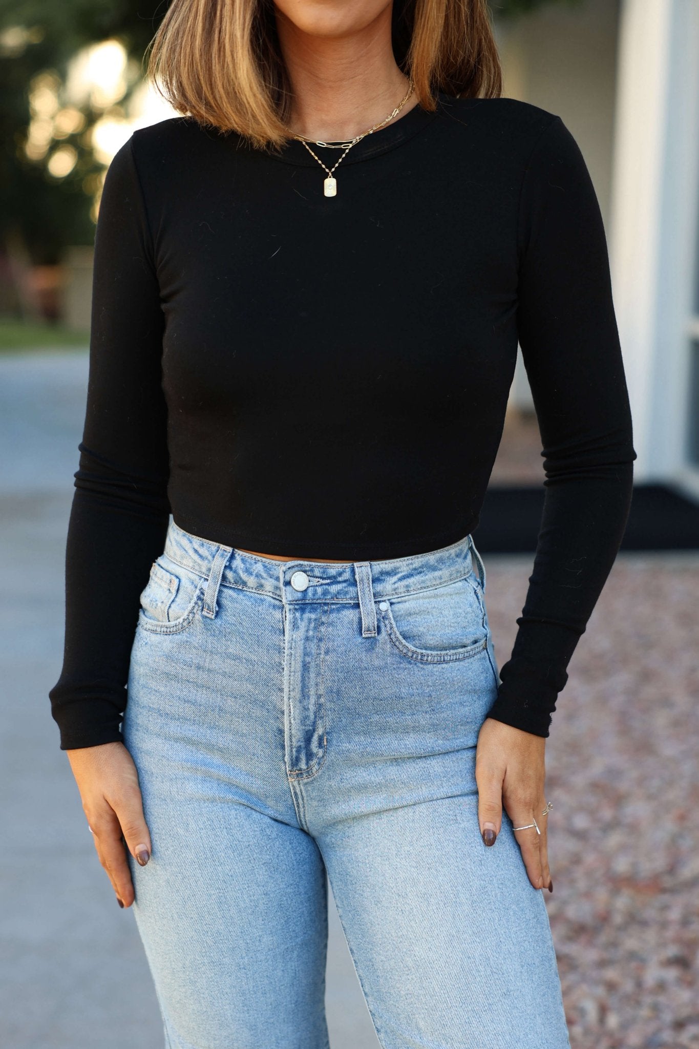 A woman wears the Perfectly Smooth Black Basic Top with relaxed fit, high-waisted light blue jeans, standing outdoors.