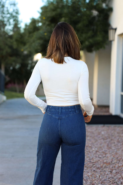 Wearing the Perfectly Smooth White Basic Top and relaxed-fit blue jeans, a woman stands outdoors facing away from the camera.