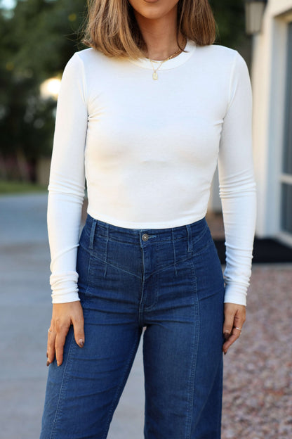 Woman in a relaxed fit, long-sleeve Perfectly Smooth White Basic Top and high-waisted blue jeans—ideal for everyday outdoor wear.