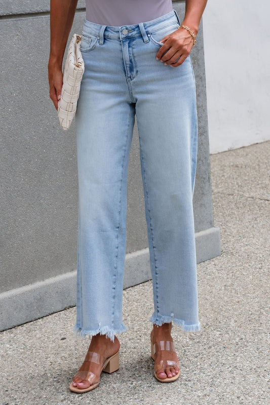 A person wearing Petra High Rise Wide Leg Jeans - Light Wash, holding a woven clutch and clear-strap heels.