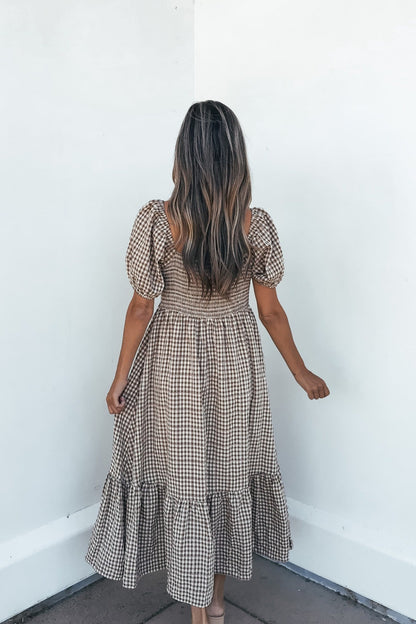 Woman in the Picnic Plaid Smock Midi Dress - Mocha faces a white corner, back to camera, on a tiled floor.