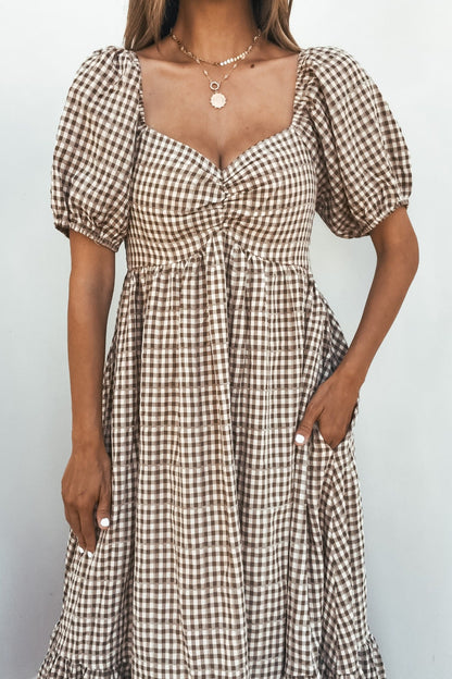 Woman in the Picnic Plaid Smock Midi Dress - Mocha, featuring puff sleeves, stands against a plain light background.