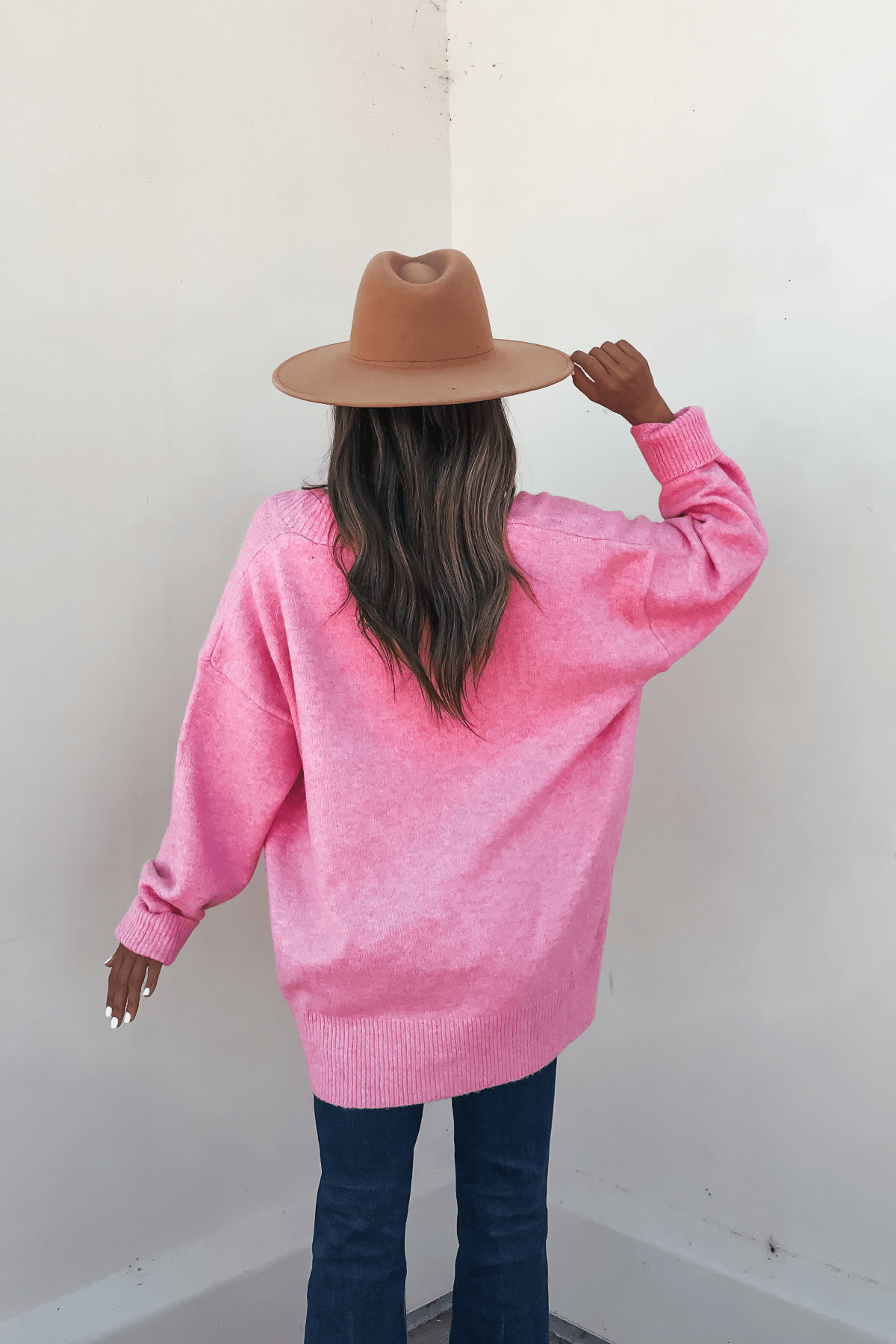Woman in a Pink Brushed Button Down Sweater Cardigan faces a light wall with her back to the camera.
