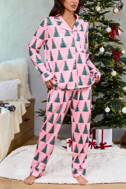 Woman in a Pink Christmas Tree Print Pajama Set - FINAL SALE stands by a festive tree and gifts in a cozy living room.