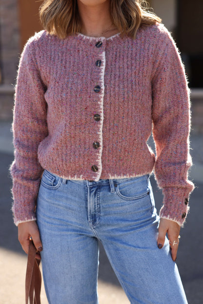 Woman in a Pink Speckled Button Down Cardigan and light blue jeans holds a brown bag outdoors.