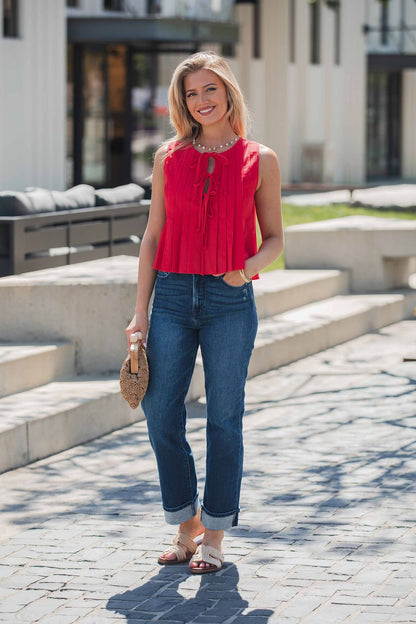 Woman outdoors in a Pleated Tie Front Top - Red, blue jeans, sandals, and a small woven bag, smiling at the camera.