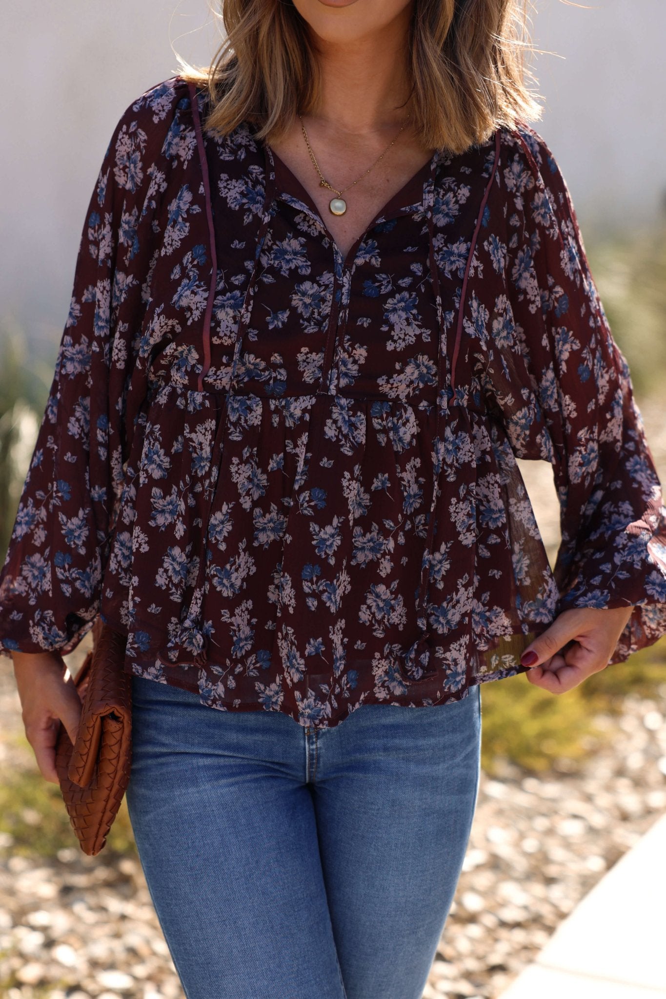Woman in the Plum Blossom Babydoll Top with blue jeans and a brown clutch—an ideal fall look for sunny days.