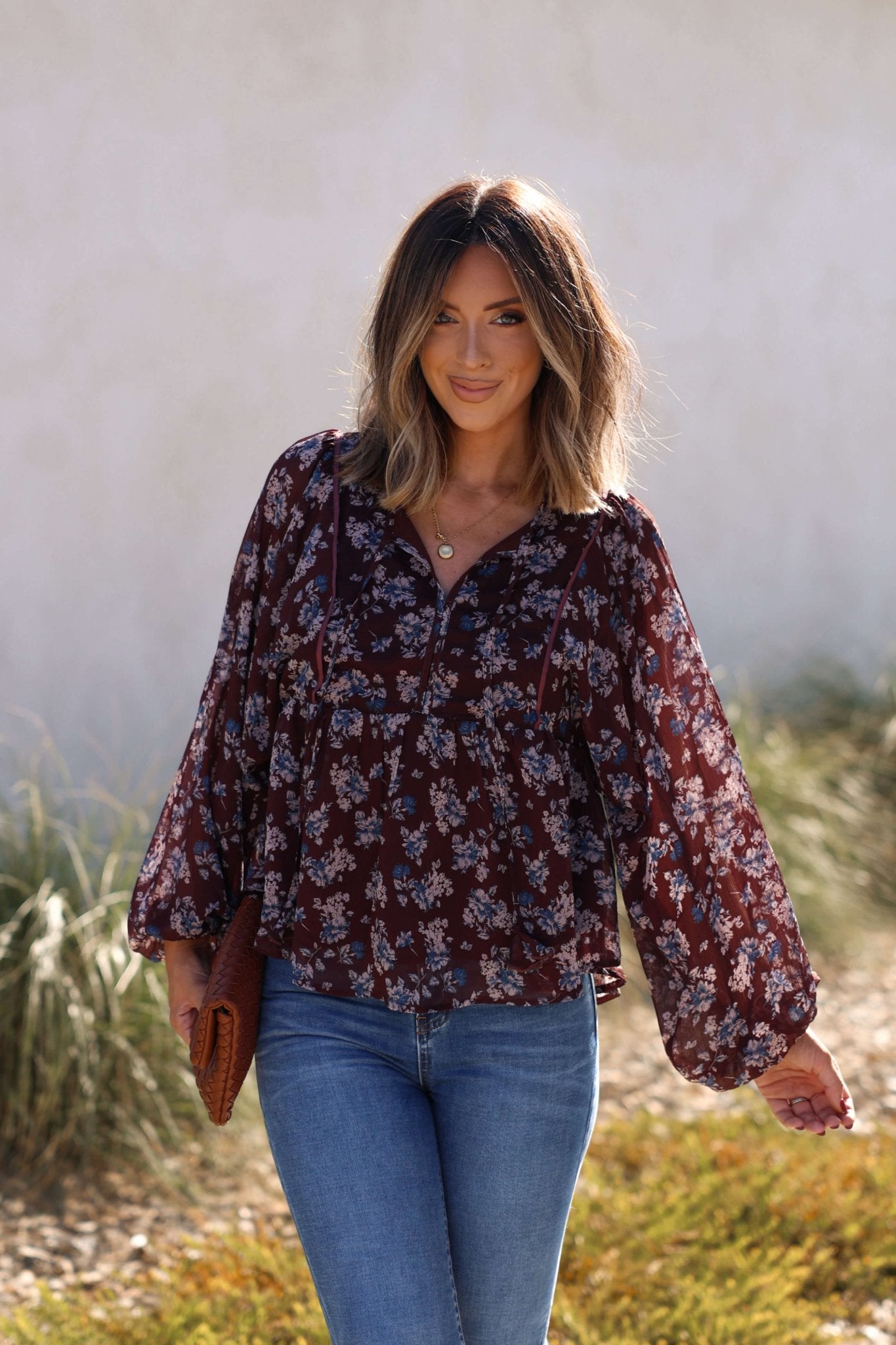 Smiling outdoors in sunlight, she wears the Plum Blossom Babydoll Top with jeans—a perfect choice for fall fashion.