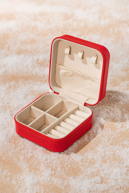 A Portable Red Leather Jewelry Box with compartments and ring slots sits on a beige surface dusted with white powder.