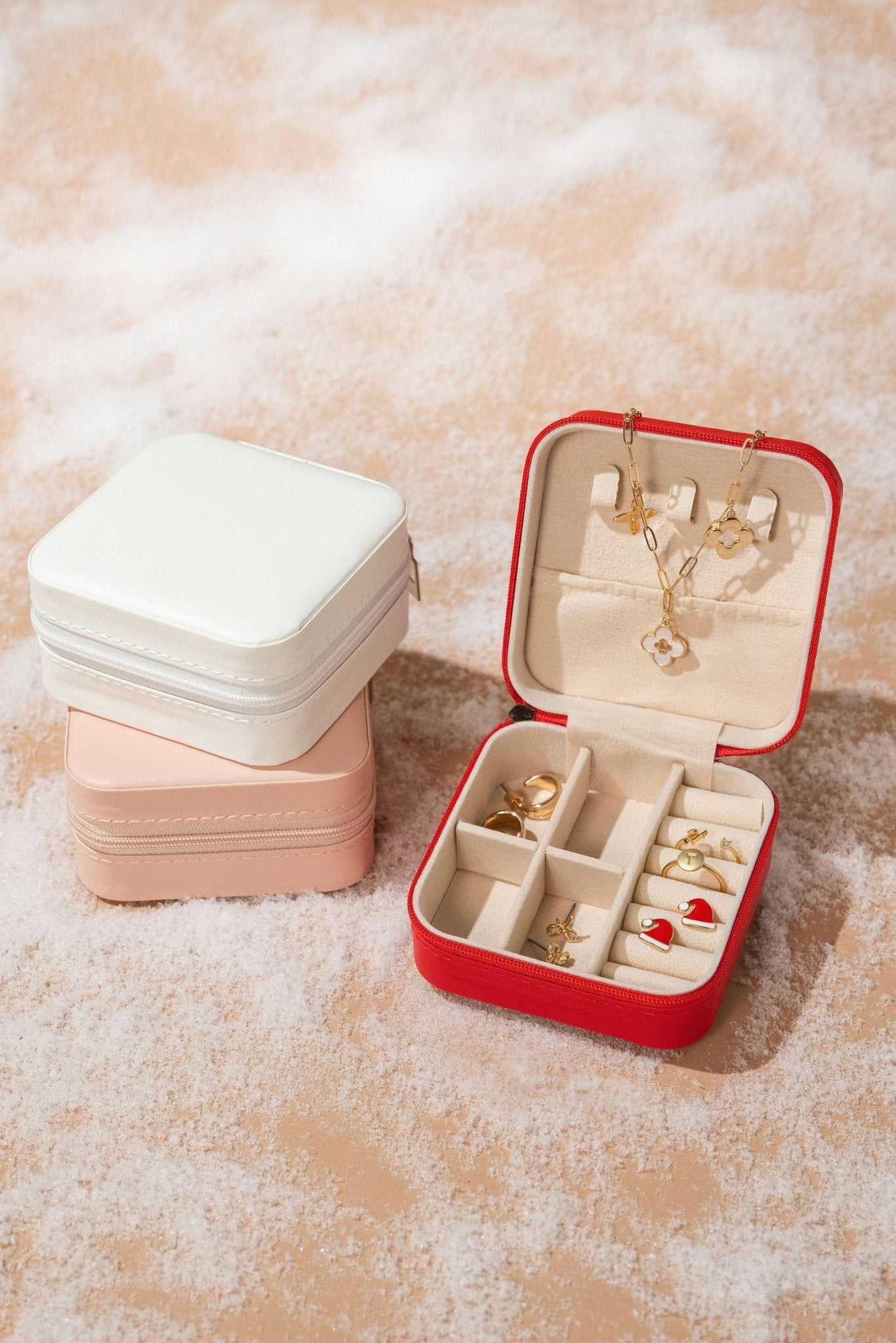 The Portable Red Leather Jewelry Box, open on a soft surface, holds gold rings, earrings, and a necklace—ideal for storage or travel.