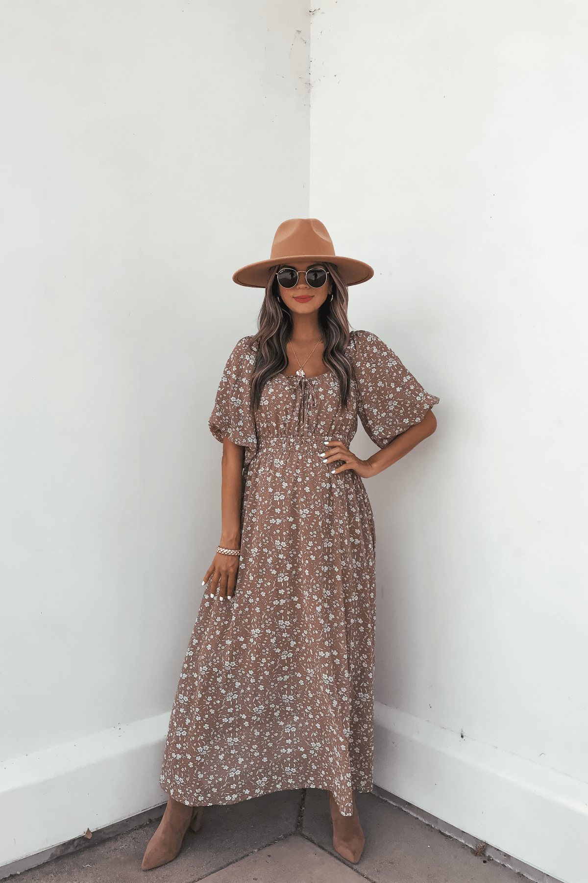 Woman in the Prairie Bloom Maxi Dress - Tan, with a hat, sunglasses, and boots, poses confidently against a white wall.