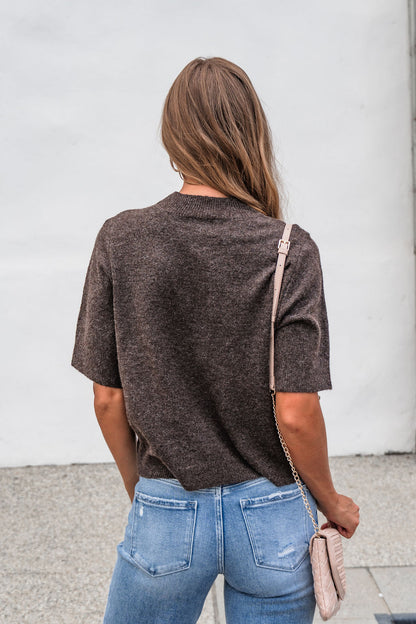 Woman with long brown hair in the Tessa Mock Neck Sweater - Brown and blue jeans, holding a beige purse, seen from behind.