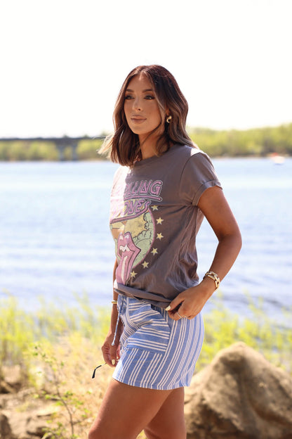 Woman in a Recycled Karma Grey Rolling Stones 1978 Graphic Tee stands by a lake outdoors, with trees and rocks in the background.