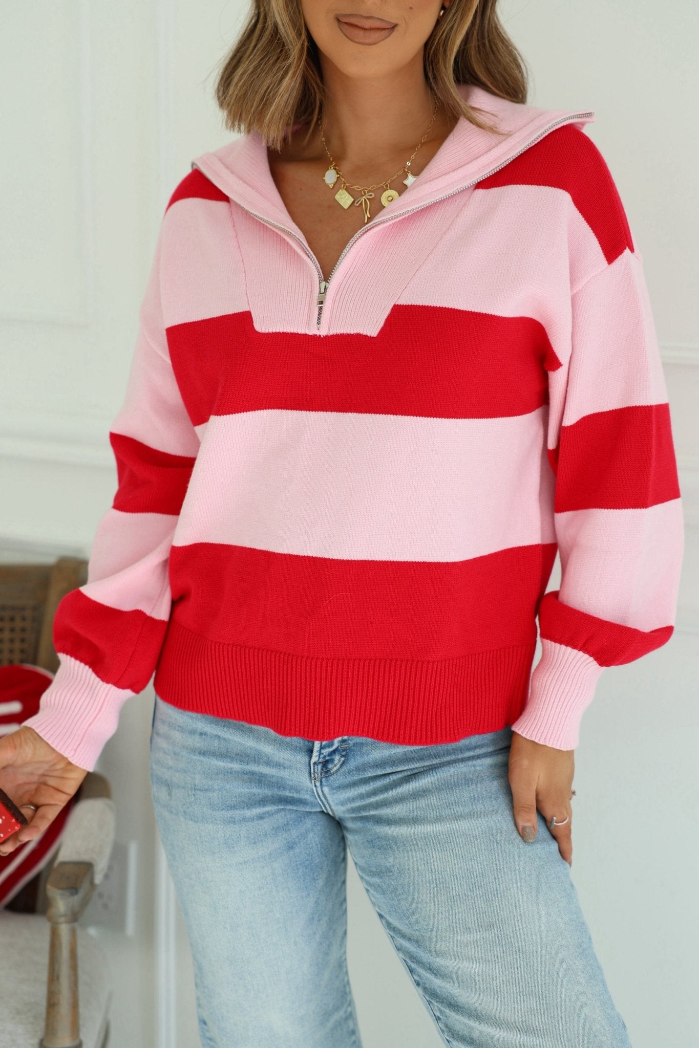 Woman in a Red and Pink Stripe Quarter Zip Sweater styled with light blue jeans, standing indoors.