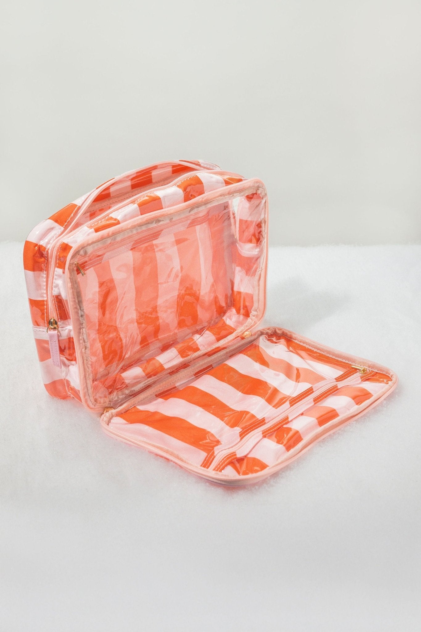 Red and pink striped travel cosmetic bag, unzipped and open, perfect as a makeup organizer on a white surface.