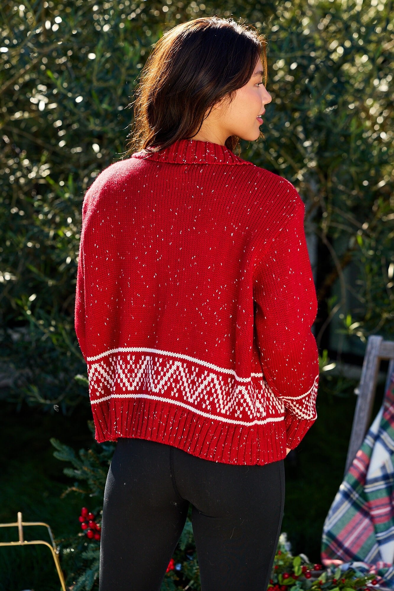 Woman outdoors in a red and white Aztec zip sweater cardigan - FINAL SALE, with black pants and greenery in the background.