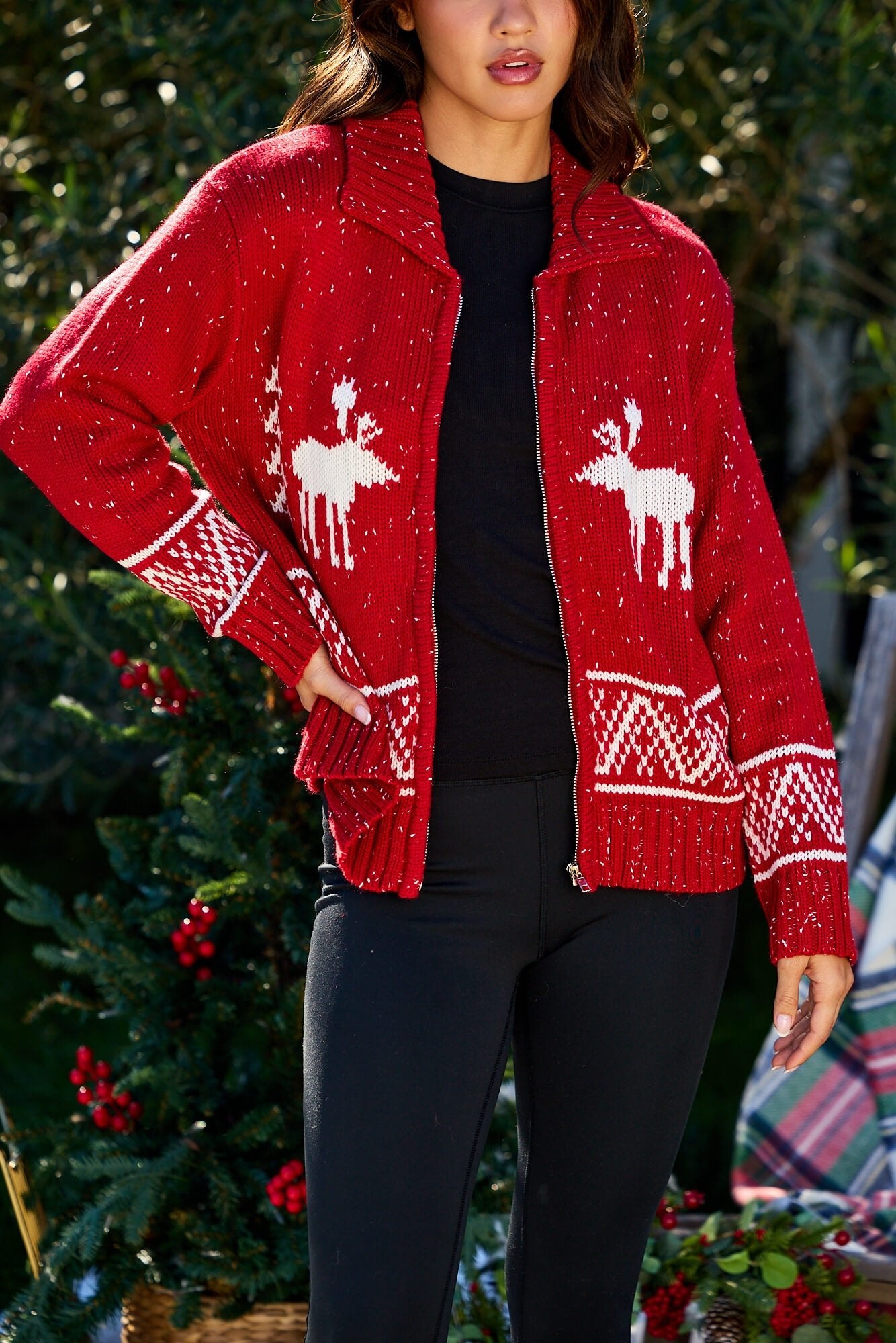 A woman in a Red and White Aztec Zip Sweater Cardigan stands by a festively decorated Christmas tree.