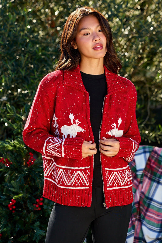 Woman in a Red and White Aztec Zip Sweater Cardigan, standing outdoors near greenery.