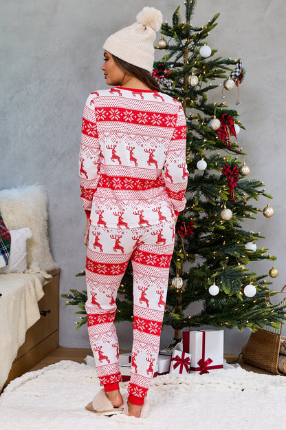 A woman in the Red and White Reindeer Print Pajama Set - FINAL SALE stands by a Christmas tree, facing away from the camera.