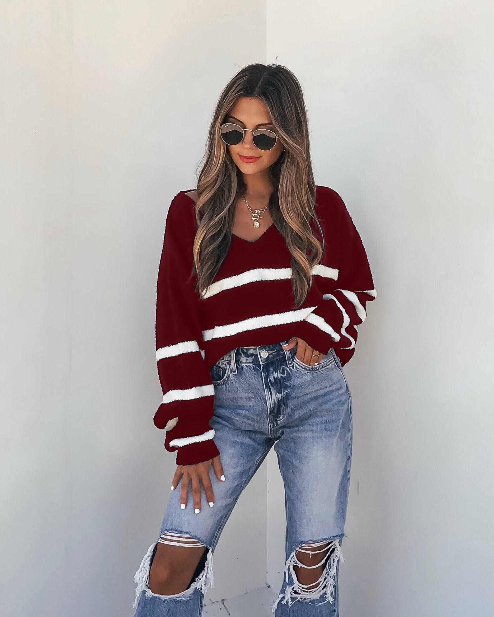 Model wears a Red and White Striped V Neck Sweater with ripped jeans and sunglasses for a chic fall look.