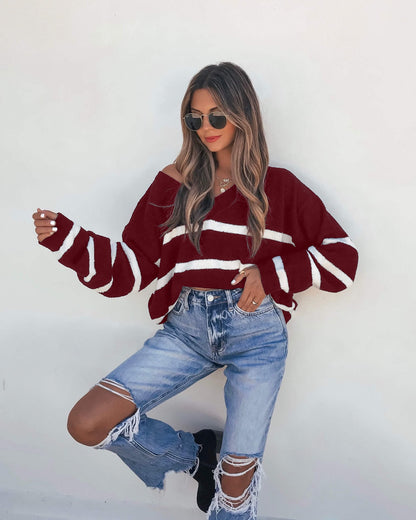 Woman in a Red and White Striped V Neck Sweater, ripped jeans, sunglasses, and black boots poses against a white wall.