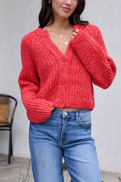 Woman in a Red Confetti Knit Buttoned Cardigan and blue jeans, standing indoors with a chair behind her.